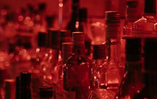 botellas de alcohol en un bar con luz roja representando el consumo social y los efectos estimulantes iniciales del alcohol