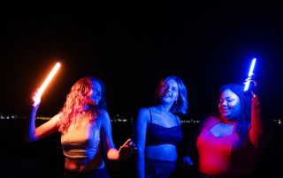 Tres noies ballen en un exterior de nit, sostenint llums de colors