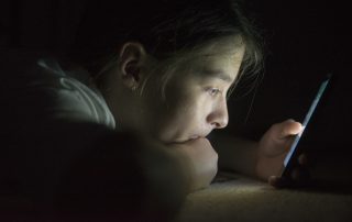 Adolescent estirat mirat un telèfon mòbil a les fosques.