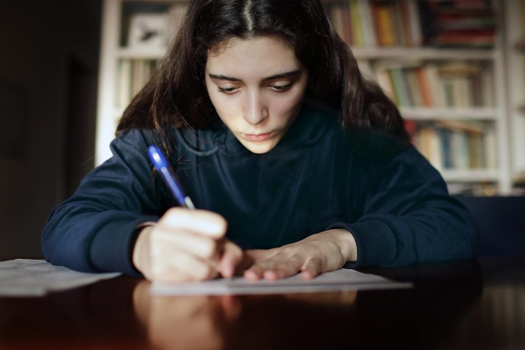 Noia adolescent escrivint en un paper