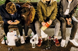Adolescents asseguts en un banc, fent botellon